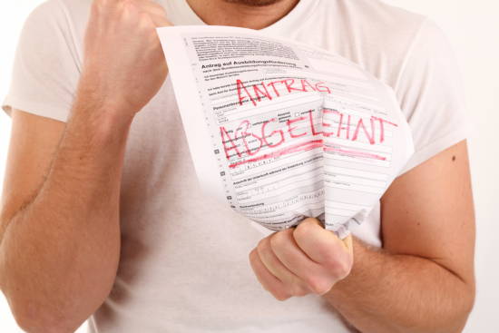 Mann mit geballter Faust der ein Antragsformular mit roter Aufschrift